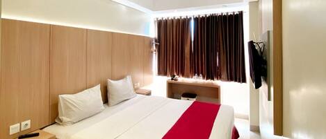 A modern hotel room with a large bed, wooden headboard, bedside tables, and a desk with a chair.