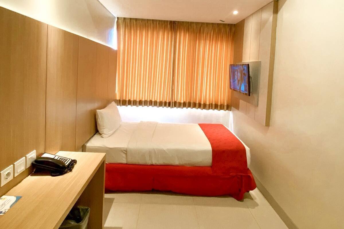 Ein Hotelzimmer mit Bett, Schreibtisch, Telefon und Fernseher an der Wand.