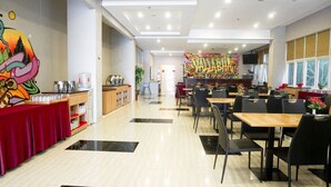 A spacious dining area with multiple tables and chairs, a buffet setup on the left, and a colorful mural on the back wall. - Brothers Inn Babarsari Yogyakarta (Depok)
