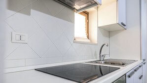 Een moderne keuken met een zwart inductiekookveld, een RVS spoelbak en een raam met zonwering.
