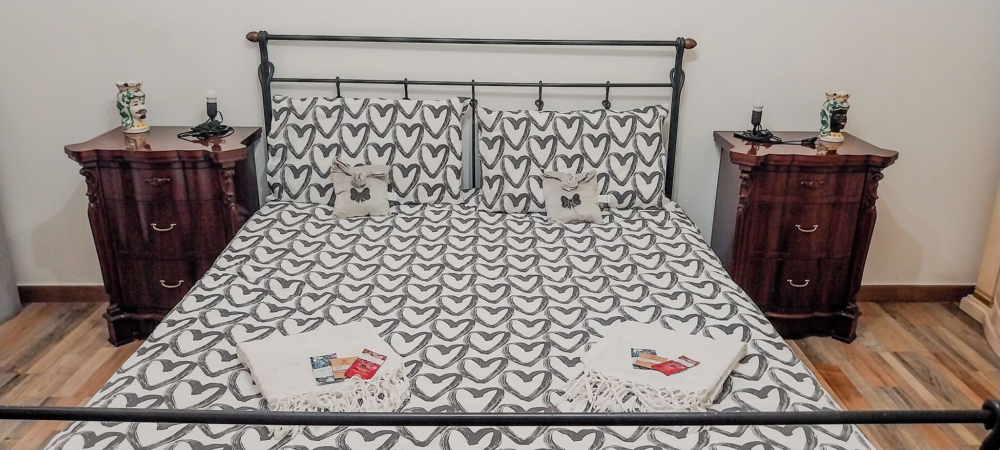Una cama con una colcha estampada de corazones, flanqueada por dos mesitas de noche con adornos.