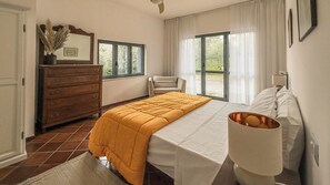 Une chambre à coucher avec un lit, une commode en bois, une chaise et une fenêtre donnant sur un beau paysage.