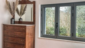 A wooden dresser with a mirror and pampas grass, a window with a view of trees, and a tiled floor. - Villa in Vigna Apartment (San Mango sul Calore)