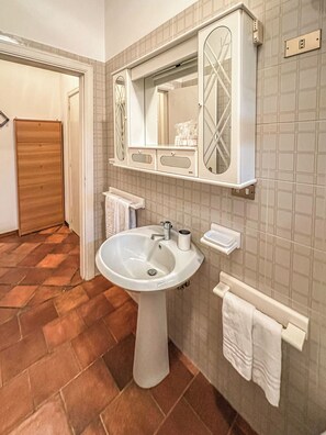 A bathroom with a pedestal sink, a mirror with a decorative frame, a towel rack, and a wooden door. - Villa in Vigna Apartment (San Mango sul Calore)