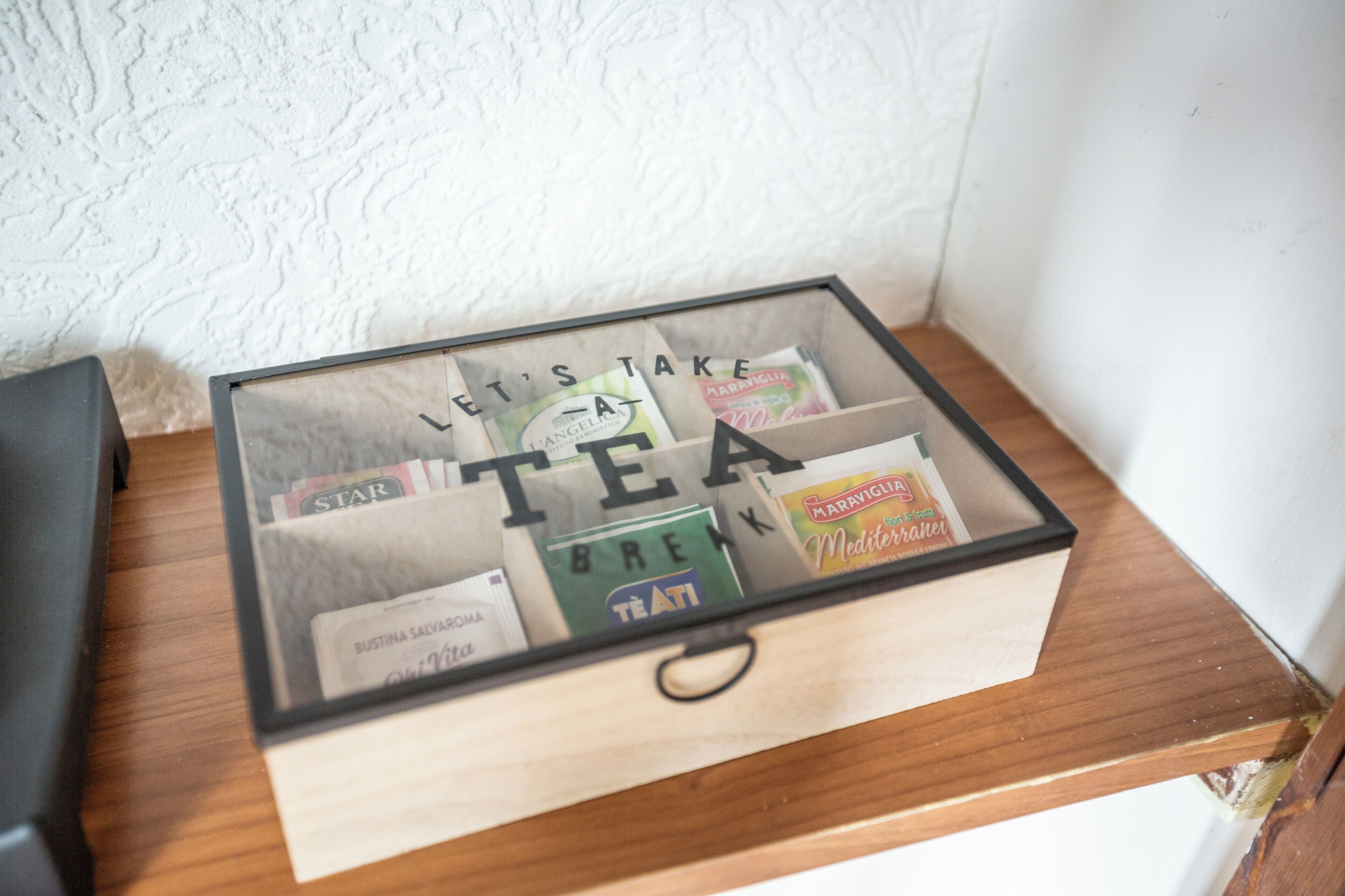 A glass box with the words "LET'S TAKE TEA" on it, containing various tea bags.