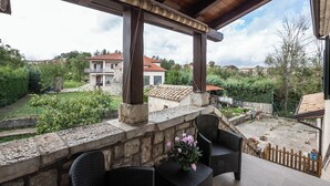 A covered outdoor area with stone walls, wicker furniture, and a view of surrounding houses. - #914 Home - Irpinia (Nusco)