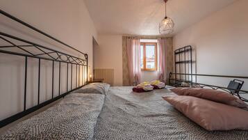 Un dormitorio con cama, mesita de noche, ventana con cortinas y lámpara colgante.