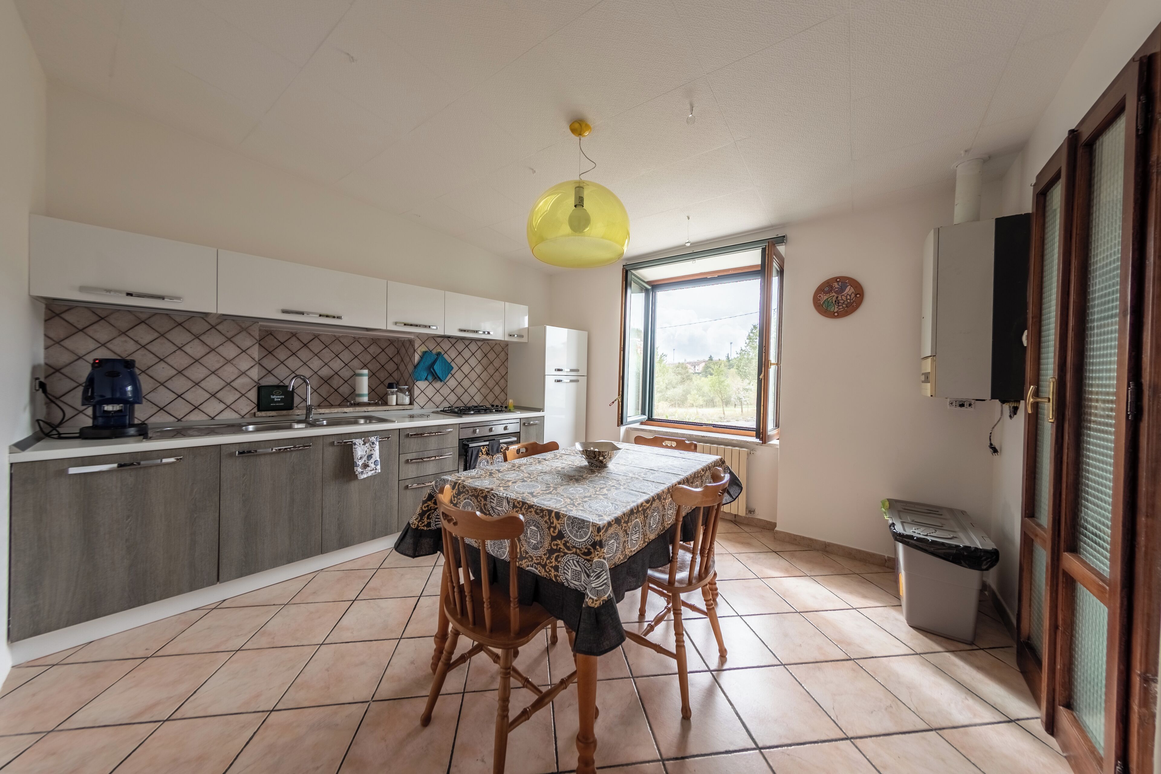 A modern kitchen with a dining table, wooden chairs, and a yellow pendant light.