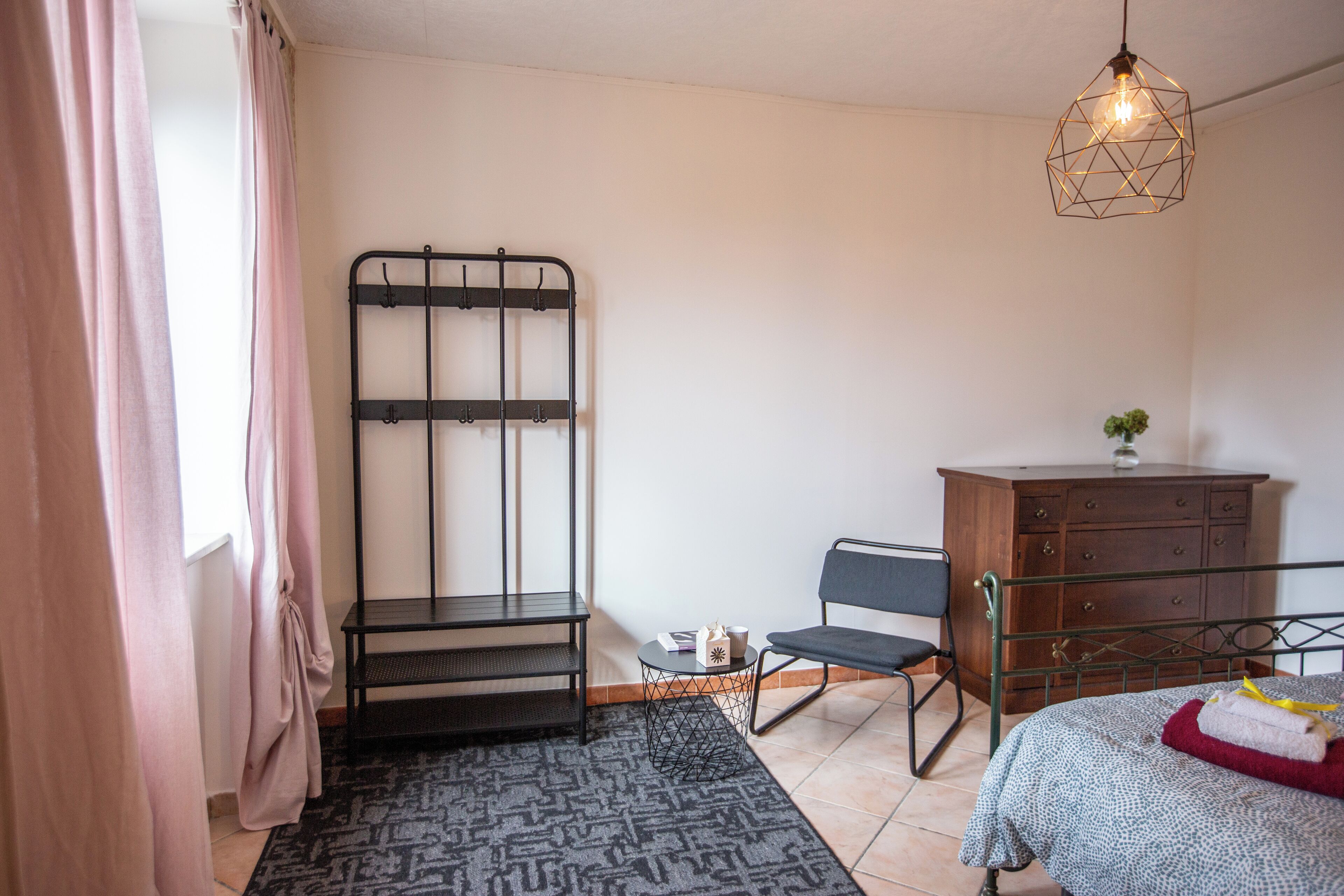 Un dormitorio con cama, escritorio, silla, cómoda y lámpara colgante.