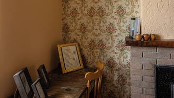 Una habitación de esquina con papel tapiz floral, una mesa de madera con marcos de cuadros, una silla y una chimenea.