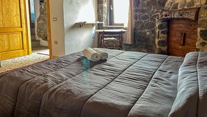 A bedroom with a large bed, a stone wall, a wooden door, and a television mounted on the wall. - Favisi Rooms (Sagama)