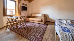 A cozy room with a wooden ceiling, a sofa, a bed, a TV, and a dining table with chairs. - Favisi Rooms (Sagama)