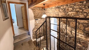 A staircase with a stone wall, wooden ceiling beams, and a metal railing. - Favisi Rooms (Sagama)