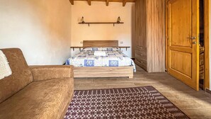 A bedroom with a wooden ceiling, a bed with a patterned bedspread, a wooden wardrobe, and a brown sofa. - Favisi Rooms (Sagama)