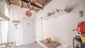 A compact kitchen with a gas stove, a microwave, and a red coffee machine. There is a small table with a basket of bread and a decorative plate on the wall. - La Casa di Sciù Sciù (Palermo)
