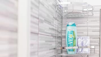 A bathroom with a shower area, a towel rack, and a shelf with toiletries.