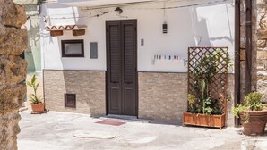 A building with a white facade, a brown door, and a small window. There are potted plants and a wooden lattice structure. - La Casa di Sciù Sciù (Palermo)
