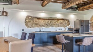A modern kitchen with a stone accent wall, built-in appliances, and a bar area with stools. - Il Casale Di John (Umbertide)