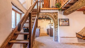 A rustic interior with a wooden staircase leading to a loft area, stone archway, and a kitchen in the background. - Il Casale Di John (Umbertide)