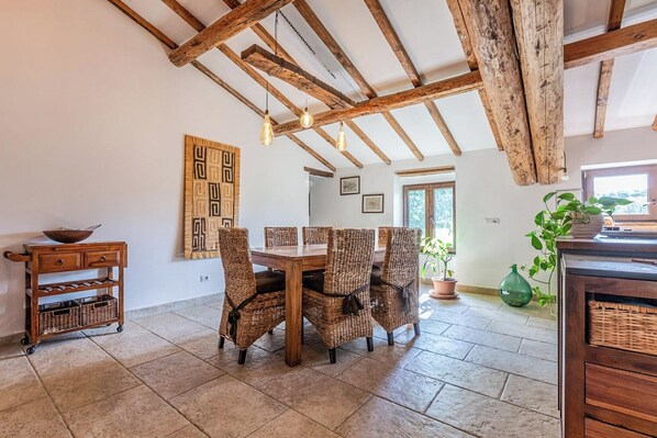 A dining area with a wooden table and wicker chairs, a wooden cabinet with baskets, and a large window with natural light. - Il Casale Di John (Umbertide)