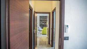 A hallway leading to a room with a radiator, a green chair, and a white wall with a thermostat. - Billotti Central Loft - Cosenza (Cosenza)