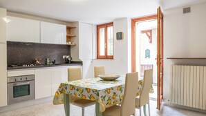 A kitchen with white cabinets, a stove, and a dining table with chairs. - Casa Vacanze Francesca (Mondolfo)