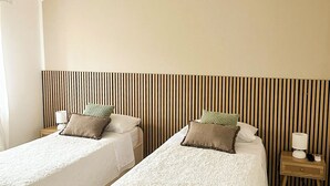 A room with two beds, a sloped ceiling, a striped wall, and a small bedside table with a lamp. - Casa Vacanze Francesca (Mondolfo)