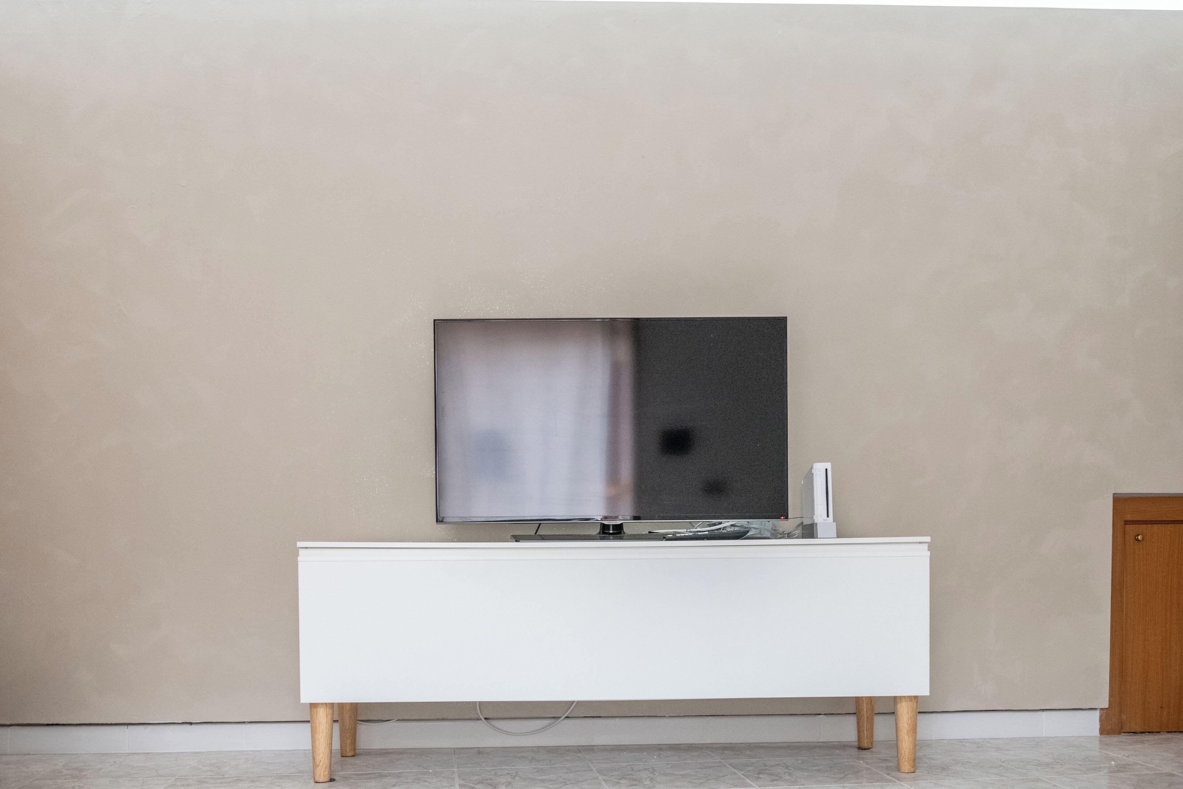 Une chambre moderne avec un meuble blanc, un téléviseur à écran plat fixé au mur et une porte en bois.
