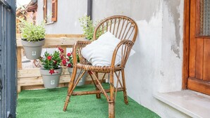 A wicker chair with a white cushion in a small outdoor area with artificial green turf, surrounded by potted plants. - Casa Vacanze Francesca (Mondolfo)
