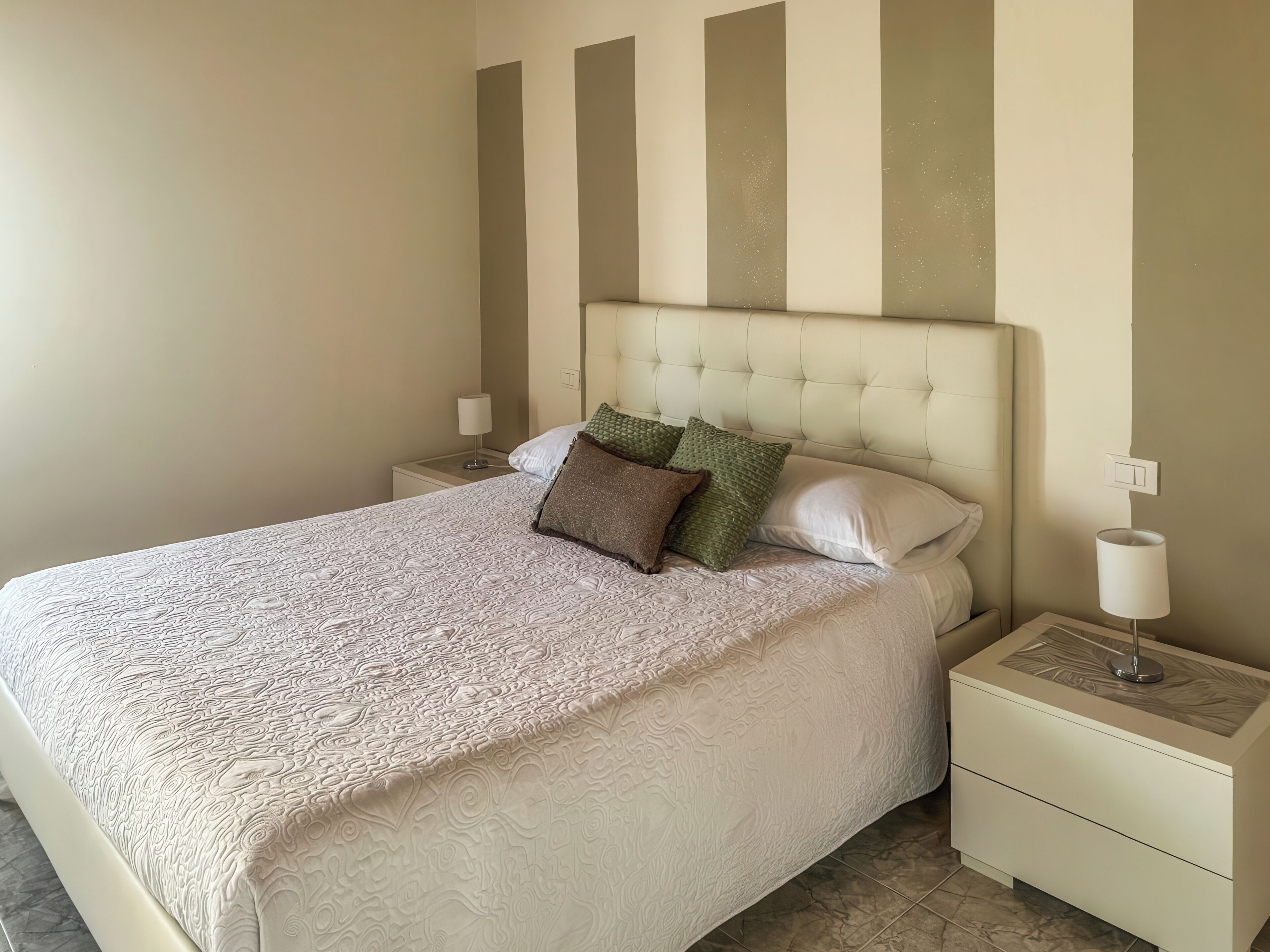 A neatly made bed with a patterned bedspread, a tufted headboard, and two bedside tables with lamps.