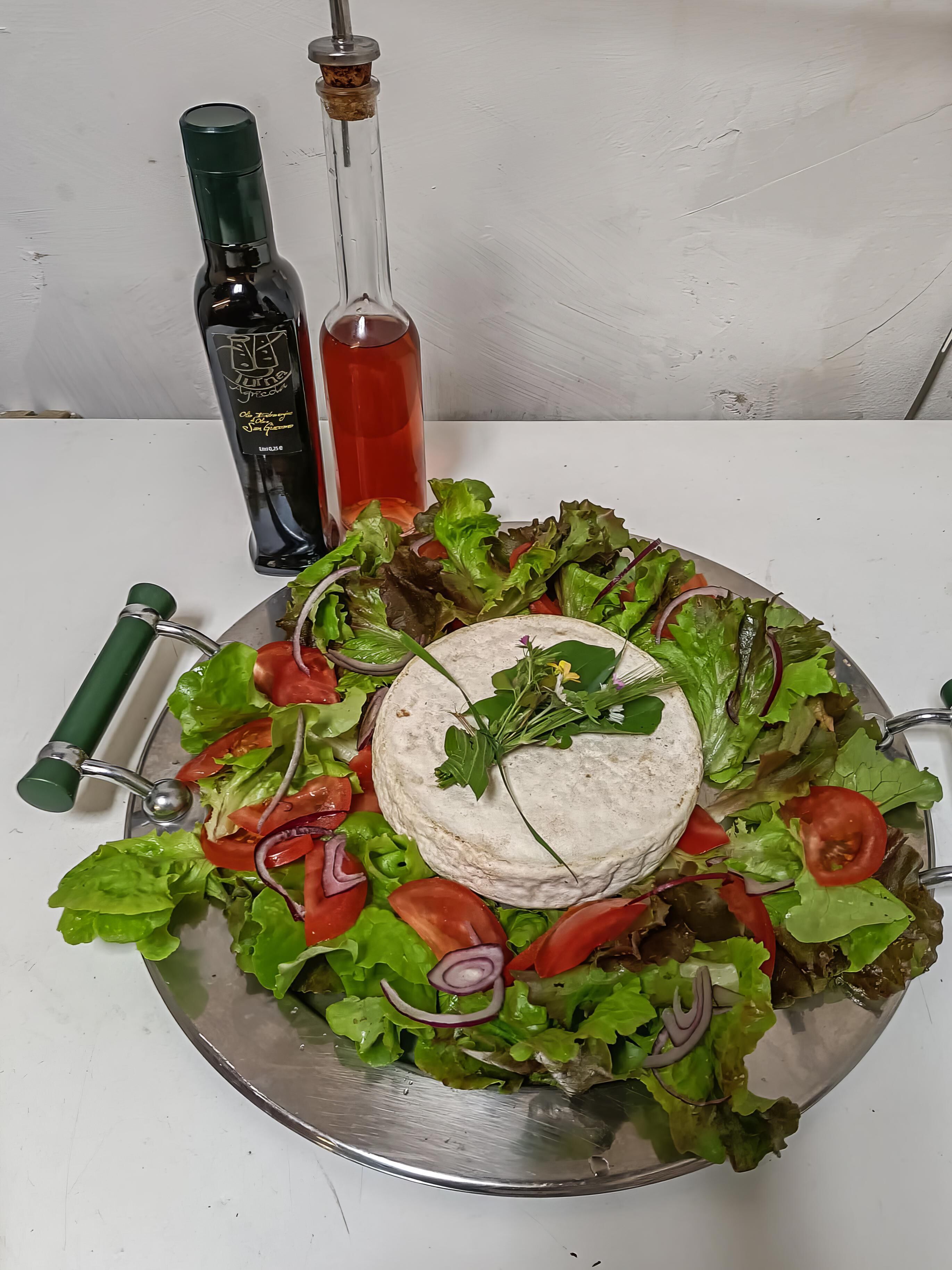 A platter of salad with a cheese ball, surrounded by various greens and tomatoes, with two bottles of olive oil in the background.