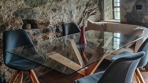 A rustic stone wall interior with a round glass table surrounded by modern chairs.
