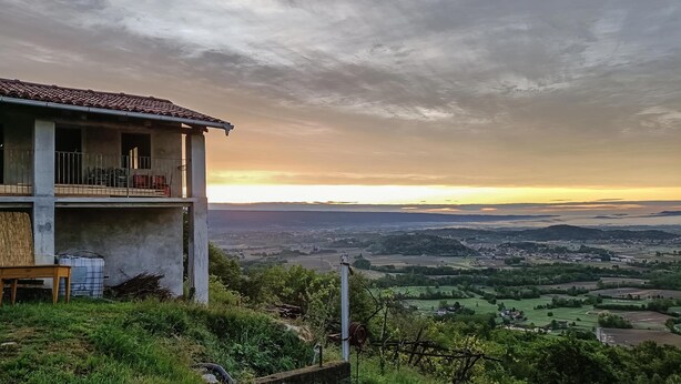 A building with a balcony overlooking a valley with fields and distant hills.