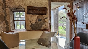 A rustic room with a stone wall, a wooden beam, a glass table, and a red vase.