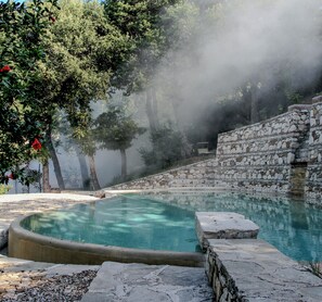 A stone pool with a stone wall and trees in the background. - Tenuta Santojanni - Irpinia (Sant'Angelo dei Lombardi)