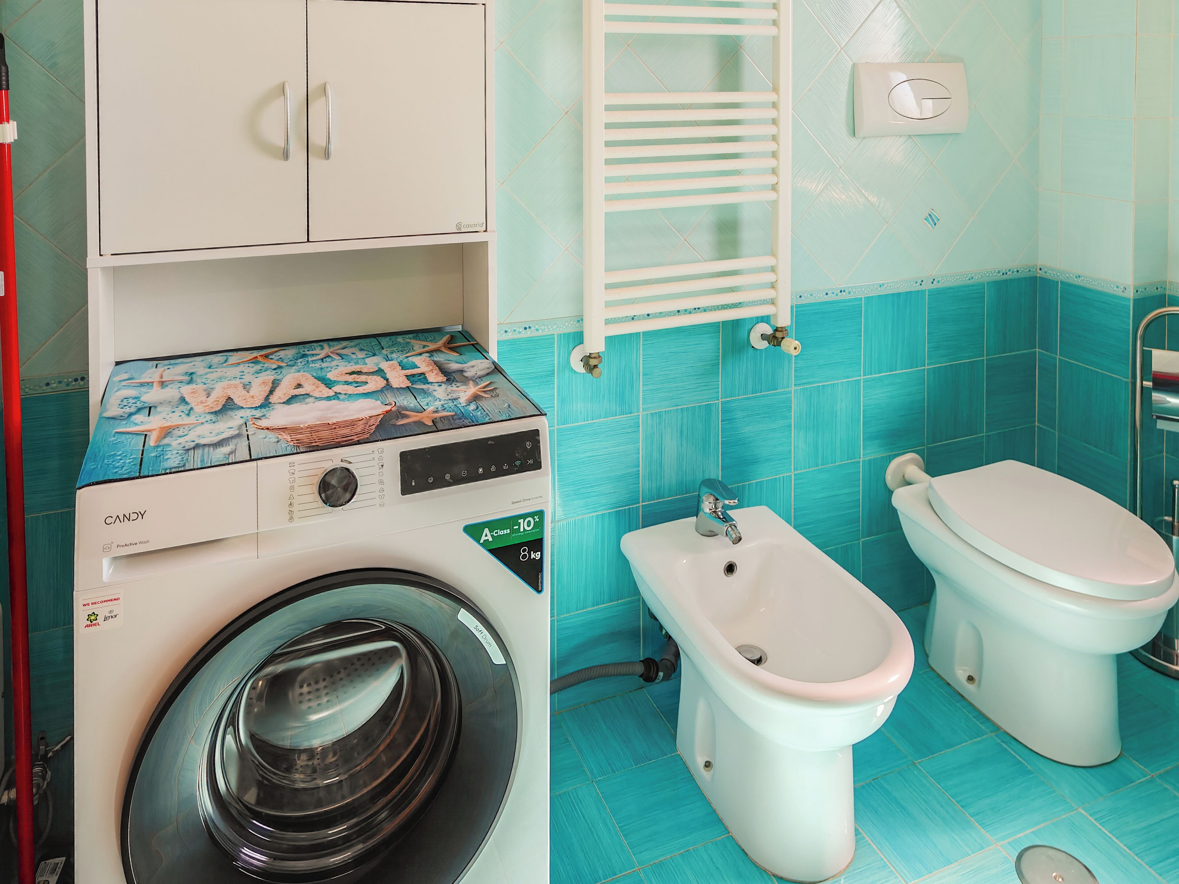 Un baño pequeño con lavadora, dos inodoros y un perchero para toallas.