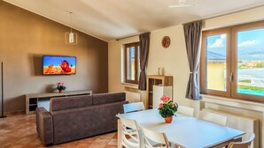 Ein Wohnzimmer mit einer Couch, einem Fernseher, einem Esstisch, Stühlen und einem Fenster mit Blick.