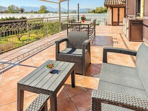 A patio with wicker furniture, a table with a potted plant, and a view of a greenhouse and mountains. - Hakuna Matata (Pontecagnano Faiano)
