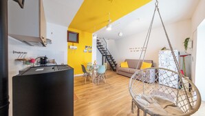 A modern kitchen with a black refrigerator, a dining area with a table and chairs, a hanging chair, and a staircase leading to a living area with a sofa and a decorative wall. - Casa Argo Guest House (Bisaccia)