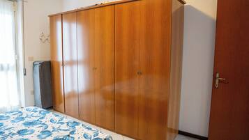 Un dormitorio con un armario de madera grande, una cama con colcha estampada y una puerta a la derecha.
