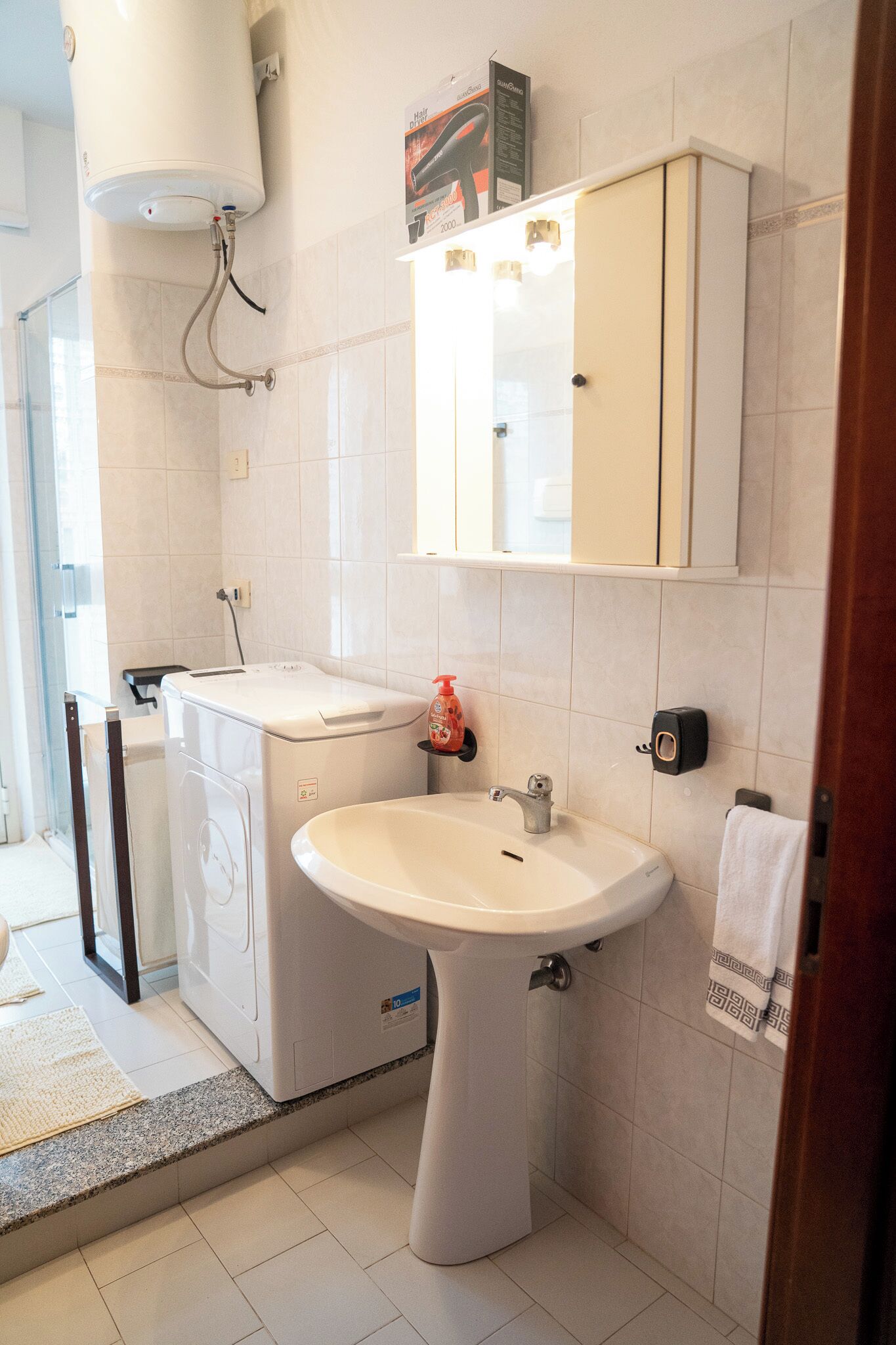 Une salle de bain équipée d’un lave-linge, d’un évier et d’un meuble de rangement.
