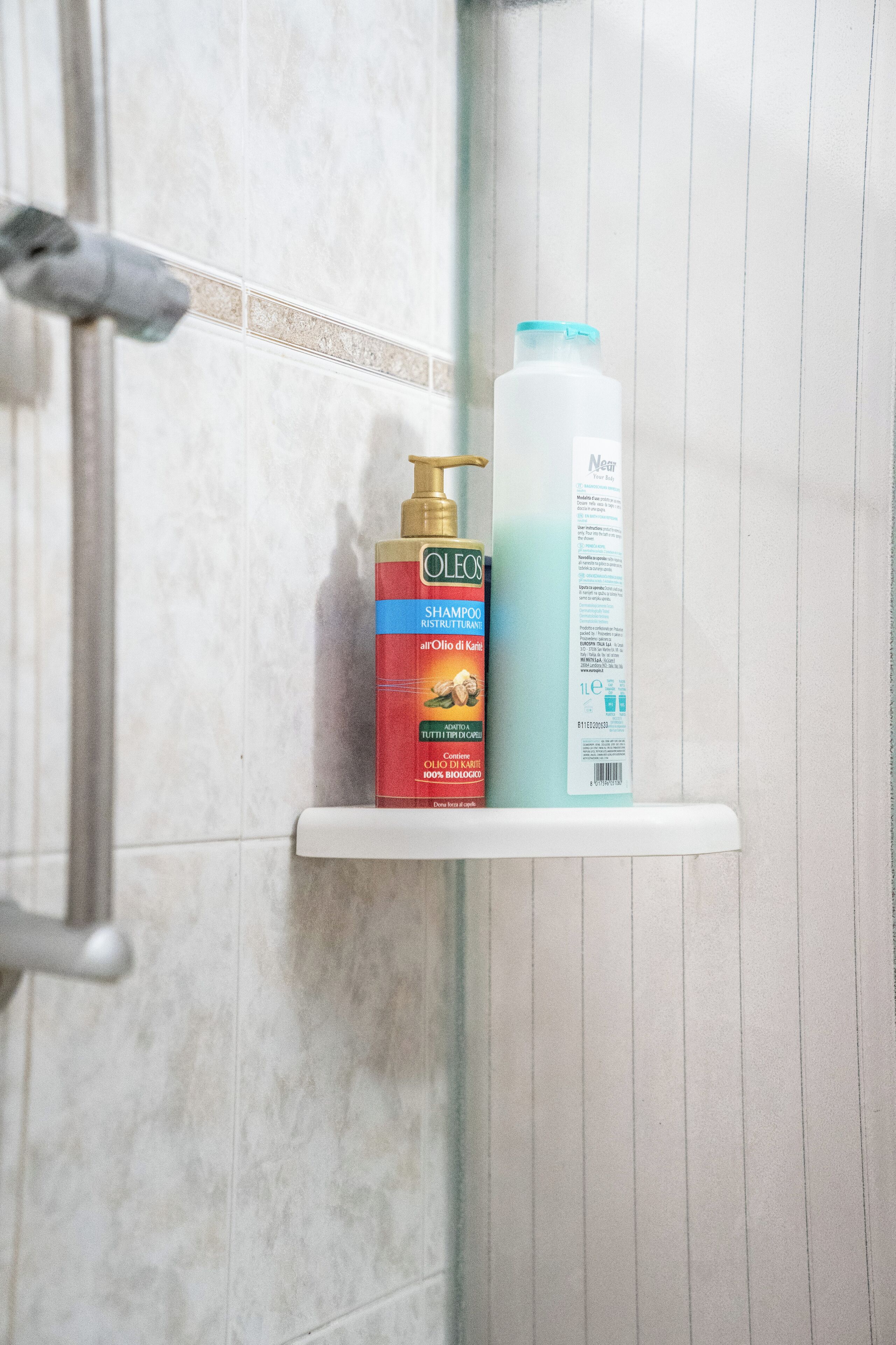 Une salle de bain avec un espace douche et une étagère sur laquelle sont posées deux bouteilles de shampoing.