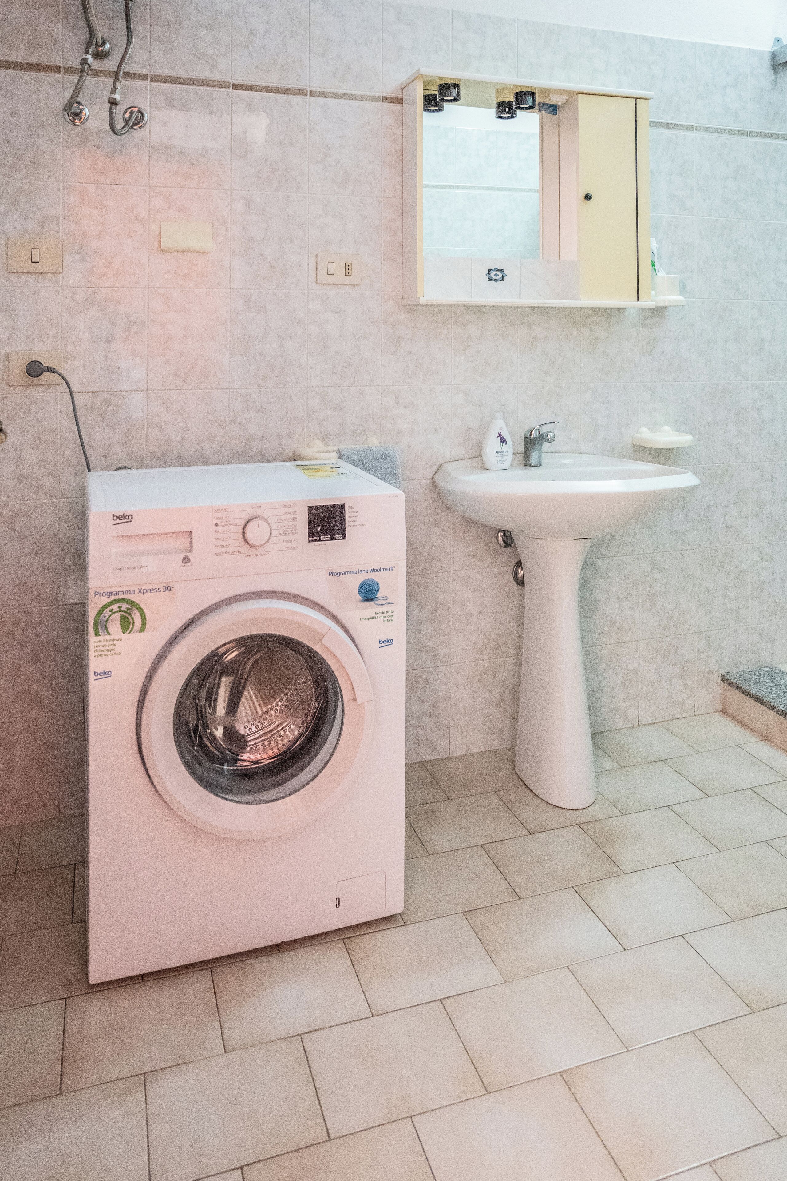Un baño pequeño con lavadora, lavamanos y espejo.