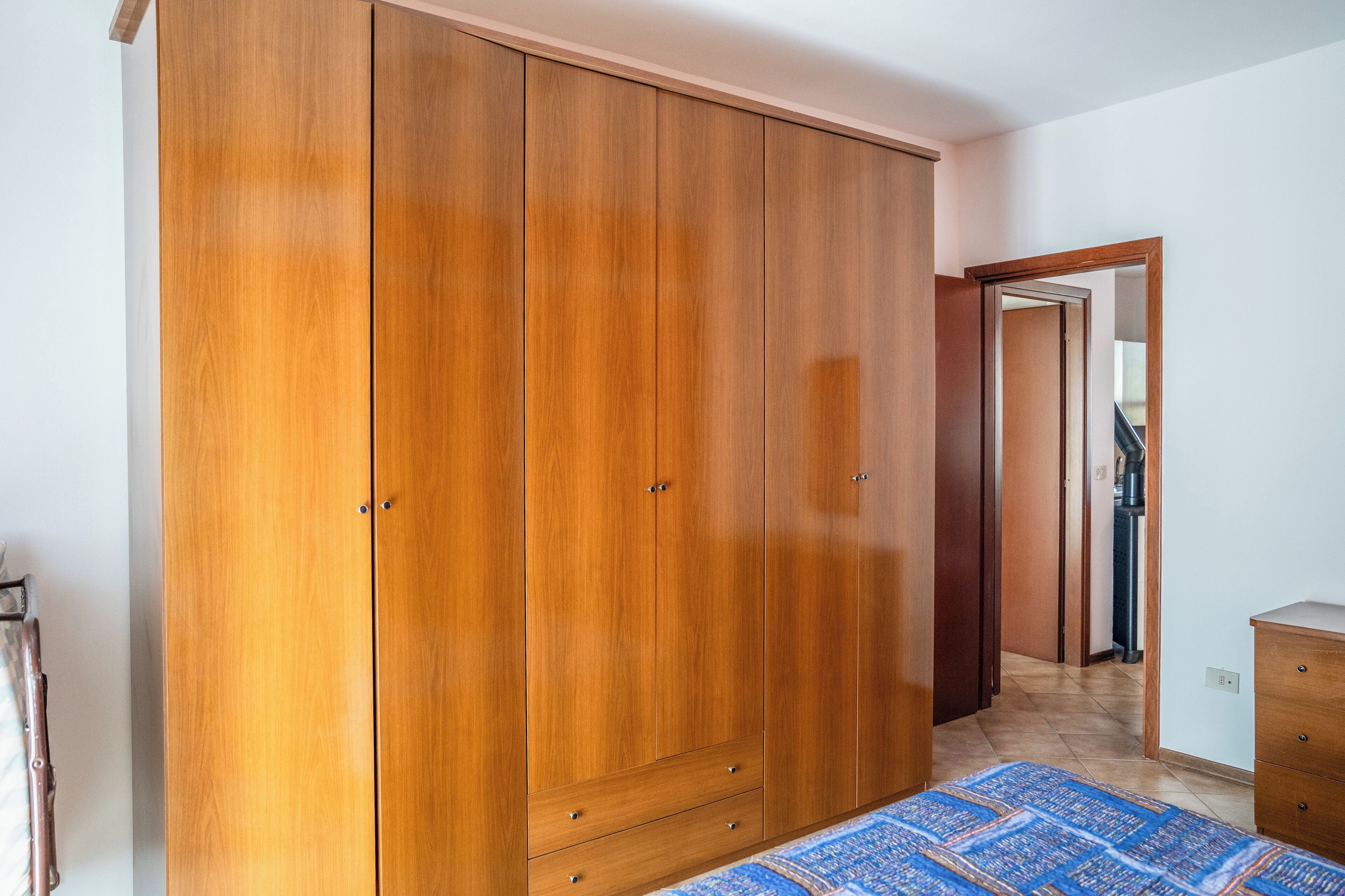 A bedroom with a large wooden wardrobe, a bed with a patterned bedspread, and a wooden dresser.