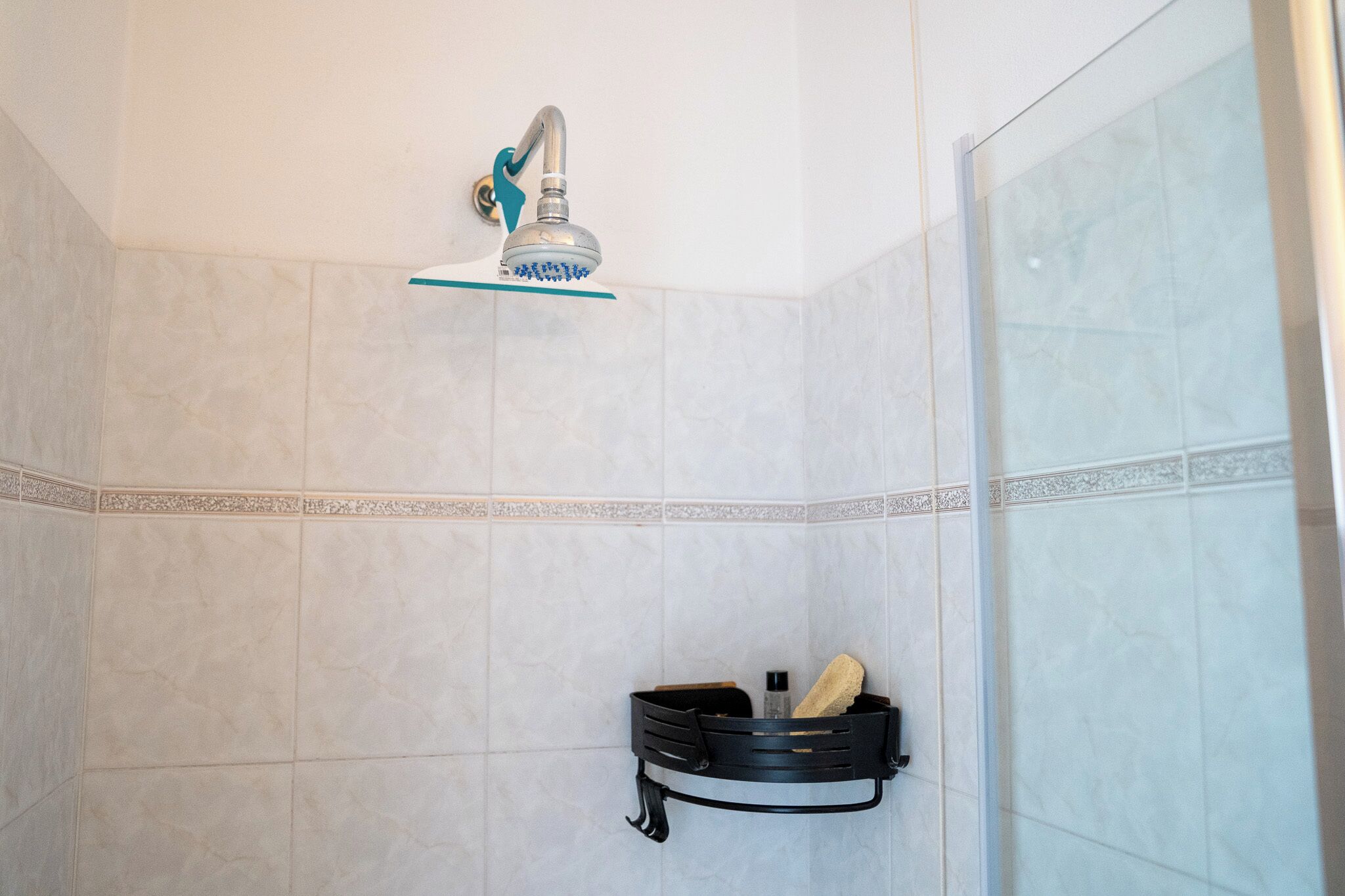 A shower with a handheld showerhead, a glass shelf above it, and a black towel rack with a towel and a bottle.