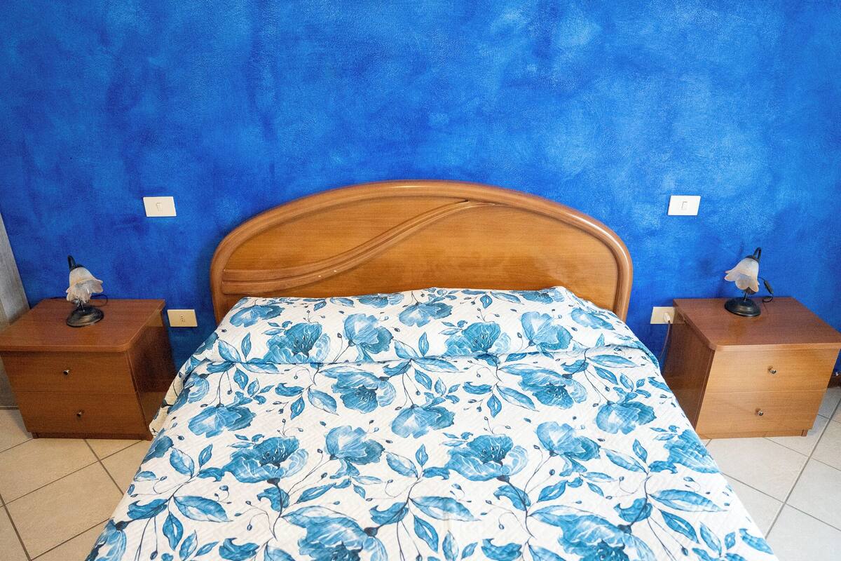 A bedroom with a wooden headboard, a floral bedspread, and two bedside tables with lamps.