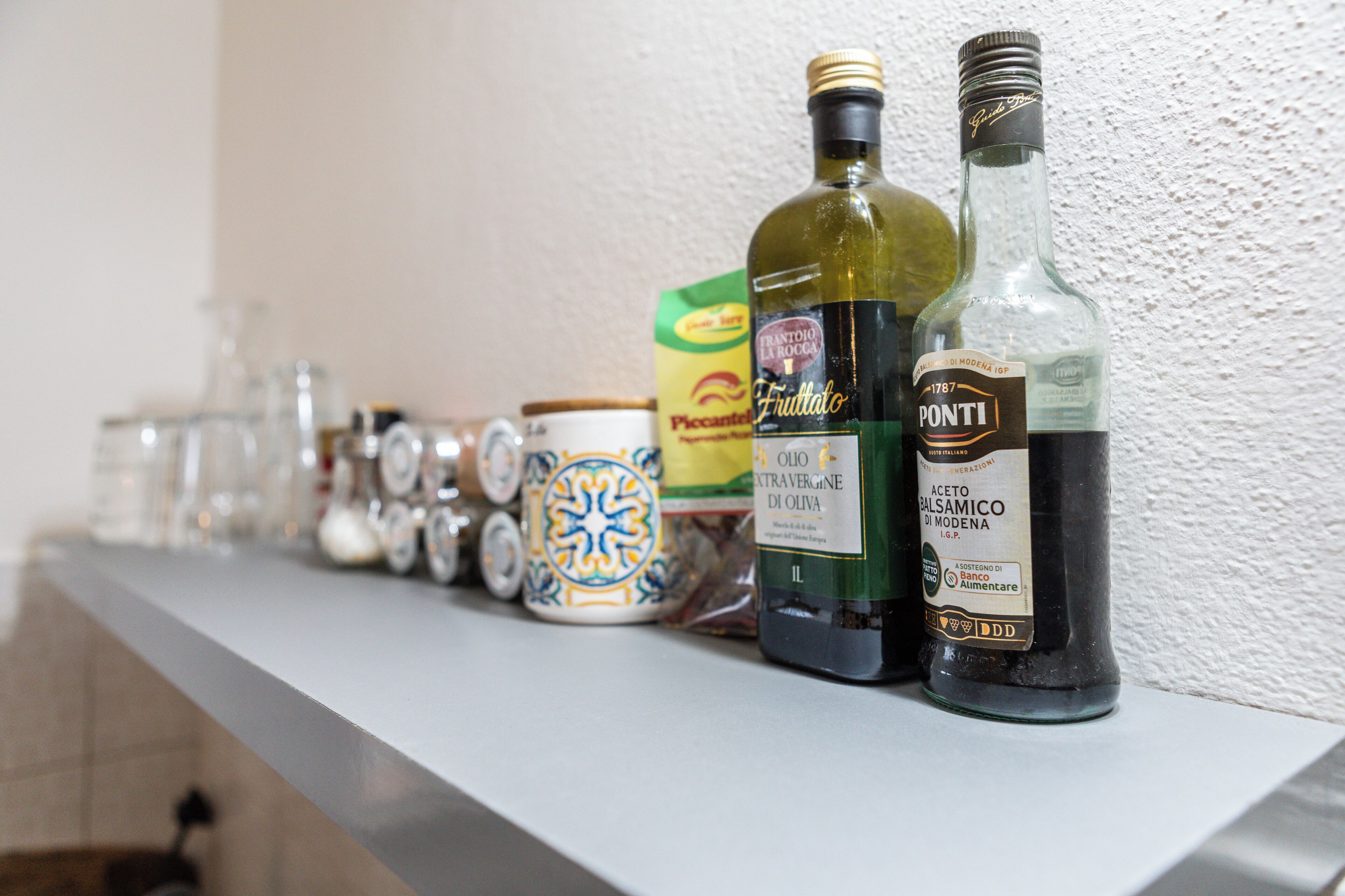 En hylla med olika flaskor och behållare, bland annat en grön flaska med etiketten ”Fruttalo”, en flaska med etiketten ”Ponti” och en burk med ett blått och gult mönster.