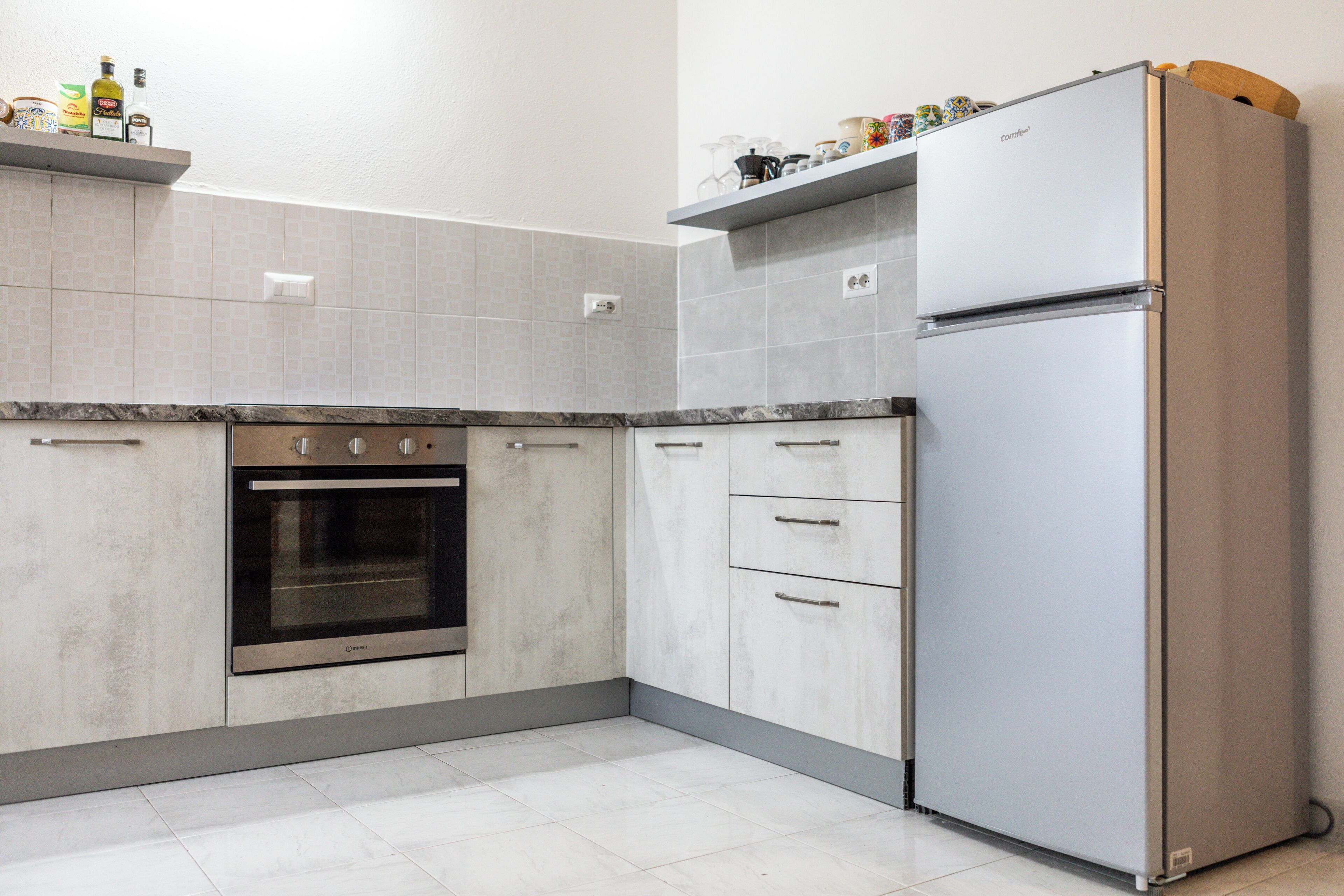A modern kitchen with a built-in oven, a stainless steel refrigerator, and grey cabinetry.