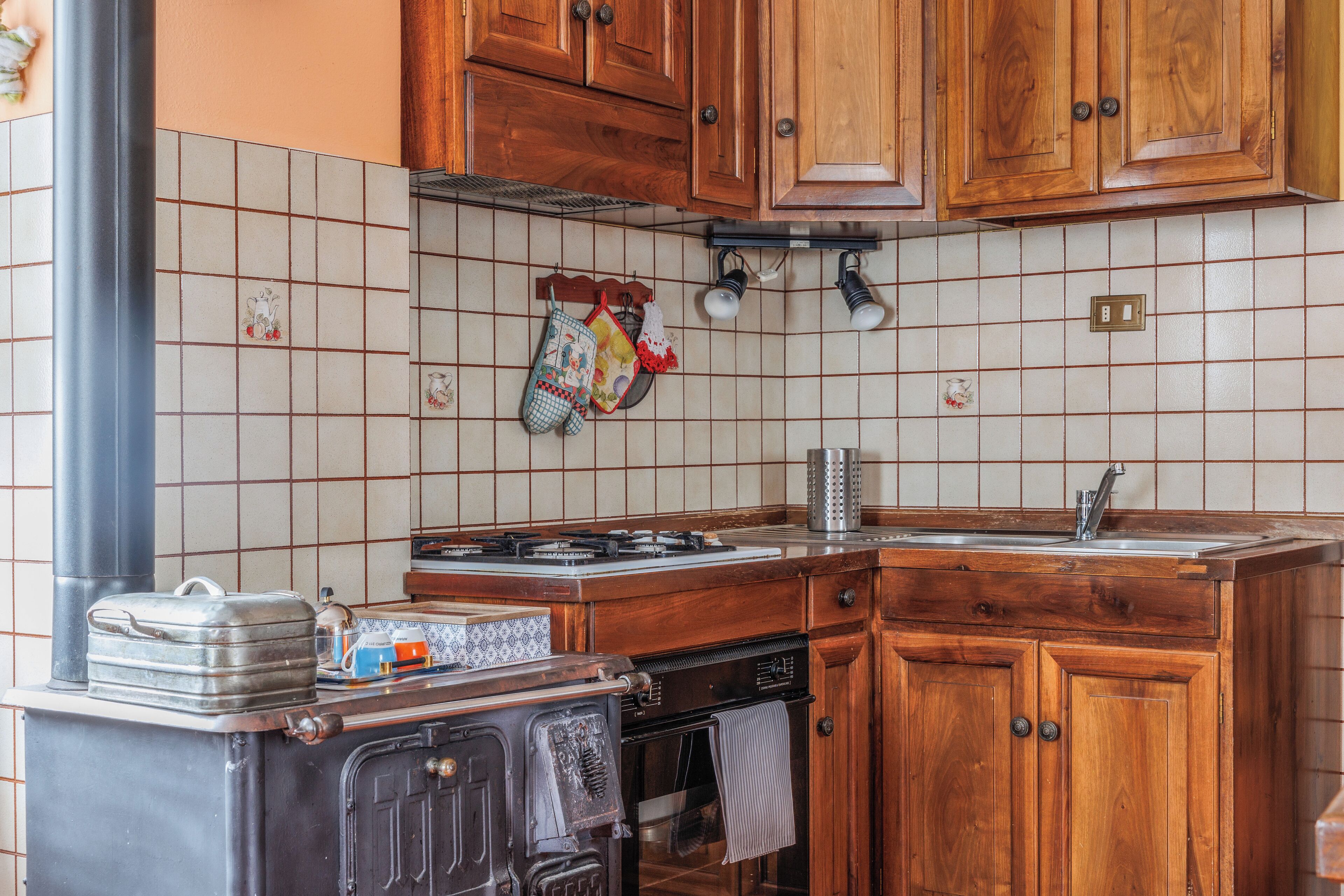 Une cuisine avec des meubles de rangement en bois, un pare-feu en carrelage, une cuisinière et un évier.
