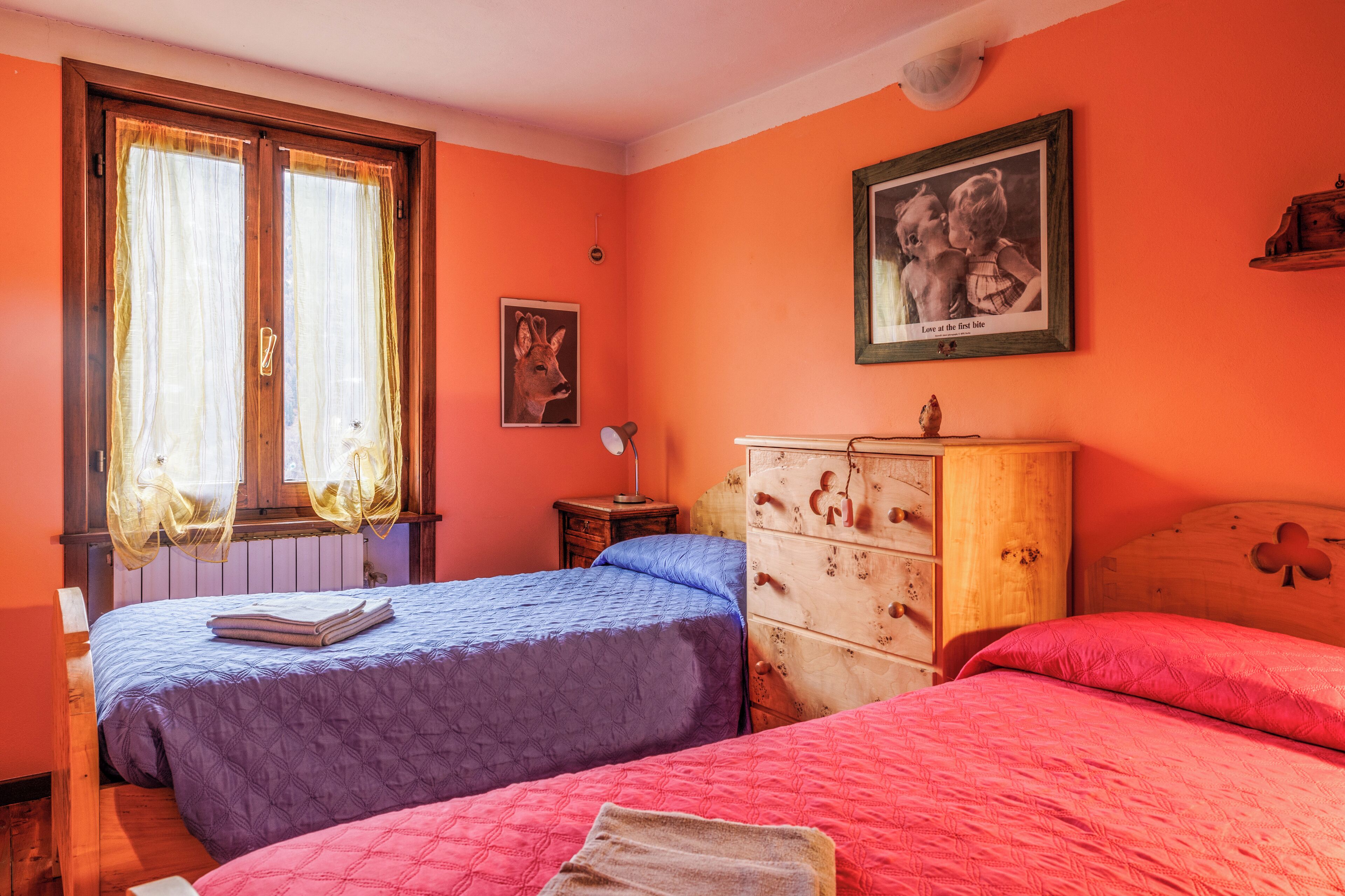 A bedroom with two beds, a wooden dresser, and a window with curtains.